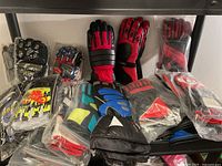 Lot of cycling gloves, most in original plastic packaging, showing a variety of colors including red, black, blue, and neon yellow accents with protective features.