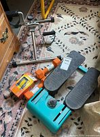 Blue Power Stepper pedal exercise device with black textured pedals, orange 8-pound dumbbells, and 2-pound ankle or wrist weights on a carpeted floor near a wooden cabinet