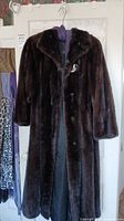 Full view of the full-length brown fur coat hanging on a white door, showing the overall length, color, and button front closures.