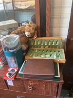 Side view of all items showing chess pieces in green felt wooden case, Gund teddy bear, UNO card box, and other game accessories