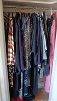 Closet view of assorted women's business casual and evening wear garments hanging on a rod, showing a variety of patterns and colors including printed and solid pieces.