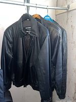 Three men's black leather jackets hanging on a rod, two appear to be size medium jackets with a smooth leather finish.