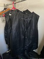 Four black leather vests hanging on hangers, showing sizes and condition.
