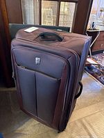Front view of brown/maroon soft sided suitcase with zipped compartments and top handle.