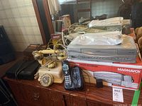 Magnavox CMWV405 VCR, vintage phones, and various electronics on surface with box visible