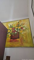 Photo of large vintage painting depicting a bouquet of yellow, red, and white flowers in a brown vase on a yellow background, signed Salina.