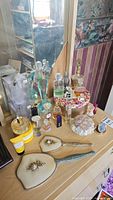 Overview of wooden dresser top with two vintage hand mirrors, various perfume bottles including some in boxes, and additional vanity items.