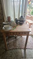 Pine table with four small drawers, shown with dishes and cups on top to illustrate size and surface area.