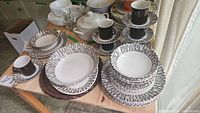 Photo showing multiple ironstone dinnerware pieces including plates, bowls, cups, and saucers all with the Espresso black and white linear pattern arranged on a table.