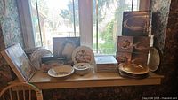 Full view of serveware and dinnerware on windowsill including boxed bowls, plates, chargers, and serving pieces