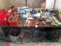 Wide view of table with multiple items including metal toolboxes, assorted hand tools in and on the boxes, and other tools spread across table