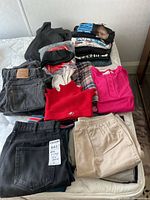Full lot of vintage t-shirts, jeans, and assorted clothing including graphic tees and pants laid out on bed.