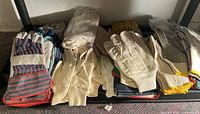 Full view of the assortment of work gloves arranged in stacks on a dark surface, showing mix of fabric and leather gloves in different colors and designs.