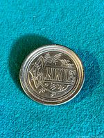 Front view of the brooch showing the engraved name 'Annie' with floral designs on the circular silver coin surface.