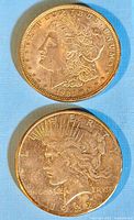 Obverse of both coins: 1921 Morgan dollar (top) and 1922 Peace dollar (bottom) on blue background