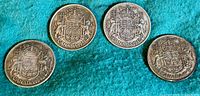 Four Canadian 50 cent coins arranged on blue fabric showing front design with coat of arms and year 1940, 41, 42, 43