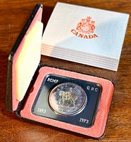 1973 silver dollar coin in vintage presentation box showing coin in black plastic holder with red velvet lining and outer white cardboard sleeve with Canada crest