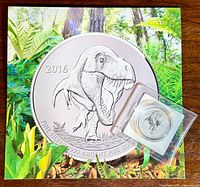 Overall photo of the quarter oz pure silver T-Rex coin in original protective plastic packaging placed on top of a colorful card with enlarged coin image.