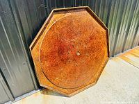 Full view of the antique octagonal crokinole board game leaning against a wall, showing the wood grain surface and condition.