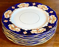 Stack of 8 Royal Albert dinner plates showing decorative cobalt blue and gold floral border with scalloped edges.