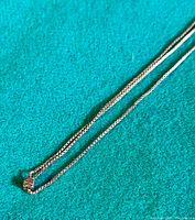 Image showing the silver box chain with sliding cube bead on a teal surface, illustrating chain design and adjustable feature.