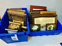 Two blue plastic bins filled with various framed prints and empty frames, showing size and material diversity