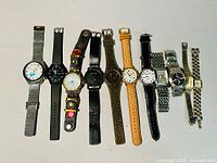 Lot of 11 assorted wristwatches laid out side by side on a white background showing variety of band types and dial styles.
