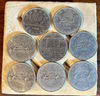 Seven Canadian dollar coins arranged on a textured cloth background, featuring dates 1969, 1972, 1973, 1975, 1976 and 1982 commemorative design.