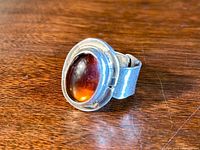 Front angled view of the silver ring showing the amber-colored glass stone set in a bezel setting on a textured band.