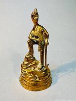 Full view of the brass miner sculpture, facing forward and showing the raised foot on the textured base, face and pickaxe details visible.