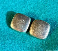 Pair of square, slightly rounded sterling silver clip back earrings on teal fabric background.