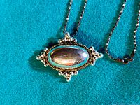 Close-up photo of the oval convex sterling silver pendant with decorative rope and bead border on a blue background