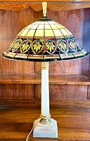Full front view of the lamp showing the Tiffany style stained glass shade and white onyx base with brass accents on a wooden background.