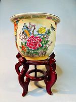 Full view of the porcelain planter on the wooden stand showing floral and bird artwork.