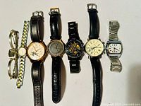 Seven wristwatches laid side by side showing a variety of designs, materials, and strap types