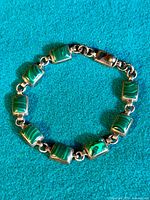 Top view of vintage sterling silver bracelet with rectangular green malachite inlays on a blue background.