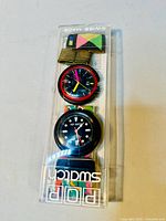 Vintage POP Swatch watches and band inside original plastic packaging, showing both analog watch faces and fabric band with multicolor geometric pattern.