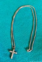 Full view of the 925 sterling silver box chain laid flat on a teal fabric background, showing entire chain length with crucifix pendant and clasp.
