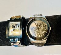 Two vintage Swatch Irony metal watches displayed on a black watch holder, front angled view showing design details and bands.