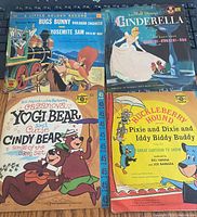Four 45 RPM vinyl records with illustrated sleeves showing Bugs Bunny & Yosemite Sam, Cinderella, Yogi Bear & Cindy Bear, and Huckleberry Hound.