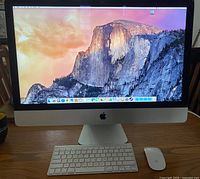 Front view of powered-on iMac with wireless keyboard and Magic Mouse on wooden surface