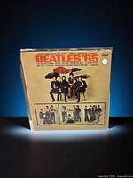 Front cover of Beatles '65 LP album by The Beatles on Capitol Records, showing band members sitting with umbrellas and multiple inset photos.