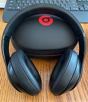 Front view of matte black Beats Studio3 wireless headphones showing cushioned ear cups and headband on wooden surface.