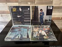 Four Billy Joel vinyl records arranged with two standing (An Innocent Man, 52nd Street) and two lying flat (Glass Houses, Turnstiles) on a black surface.