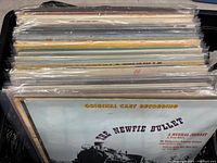 Side view showing a stack of multiple vinyl records in their sleeves in a bin with a visible cover titled 'The Newfie Bullet' original cast recording