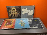 Five vinyl records arranged side by side showing front covers on a dark surface with orange background.