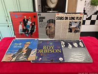 Photo of 6 vinyl records arranged in 2 rows against a blue backdrop showing album covers clearly.