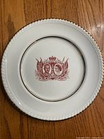 Full view of the white plate with gold trim and central maroon crest featuring portraits of Queen Elizabeth and Prince Philip.
