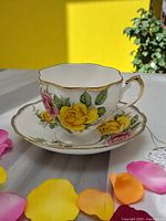Teacup and saucer set on a table with natural lighting, showing yellow and pink rose designs and gold trim
