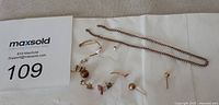 Broken chains and assorted earring parts displayed on white cloth with MaxSold lot number card